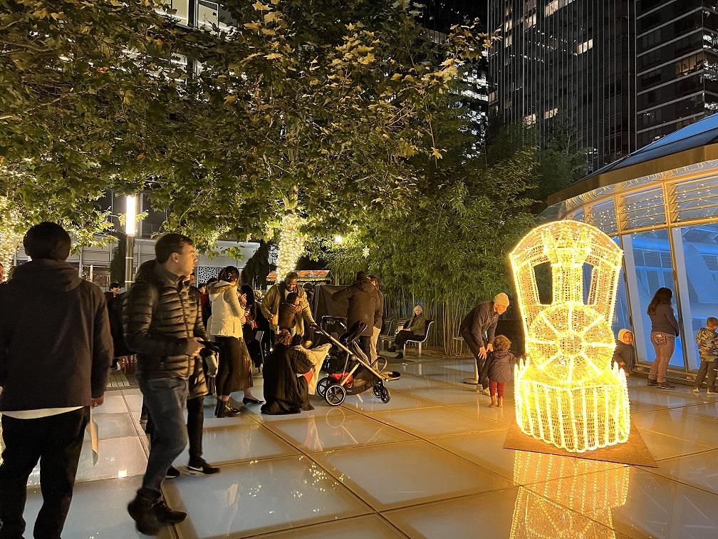 People gathered around a train made of lights at night in the TJPA's Salesforce Park on the Main Plaza.