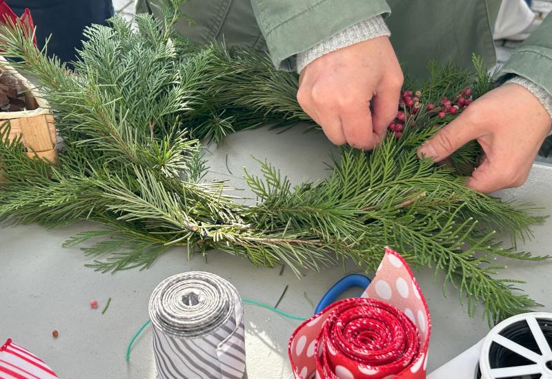 Human hands making a wreath out of pine fronds and wire.