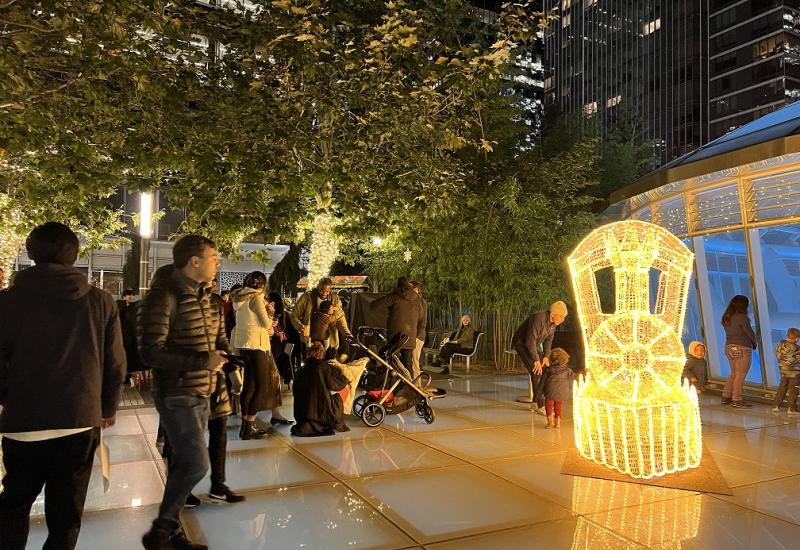 People gathered around a train made of lights at night in the TJPA's Salesforce Park on the Main Plaza.